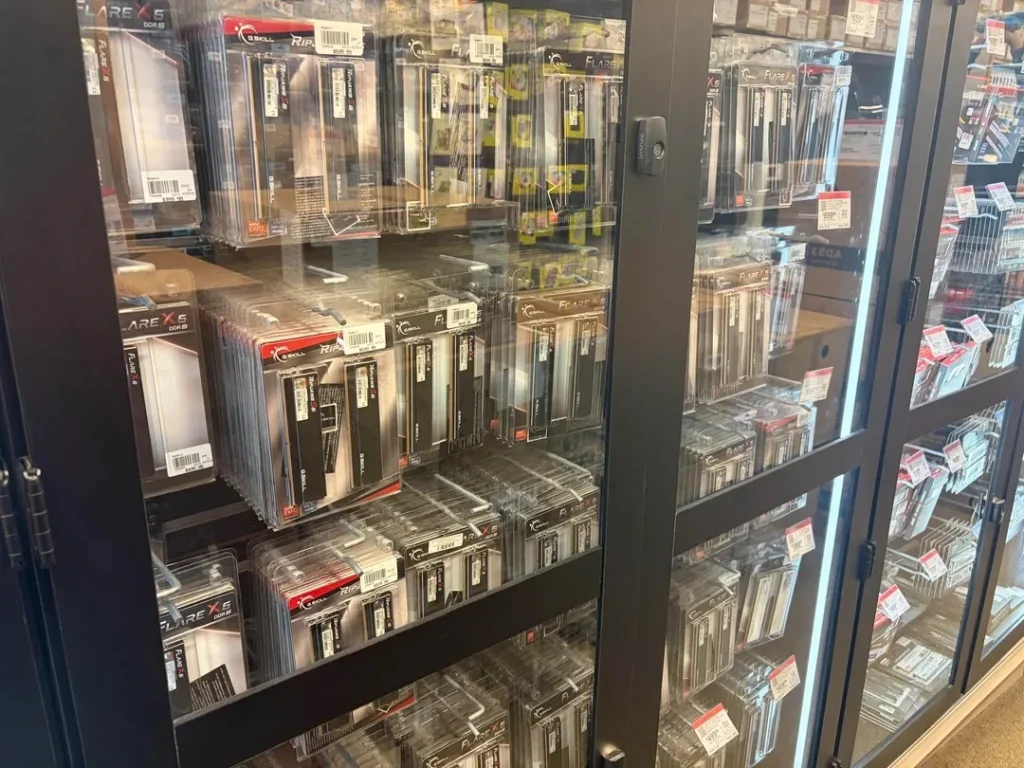Packages of G.SKILL Ripjaws and Flare X5 DDR5 RAM are displayed on shelves behind glass doors.