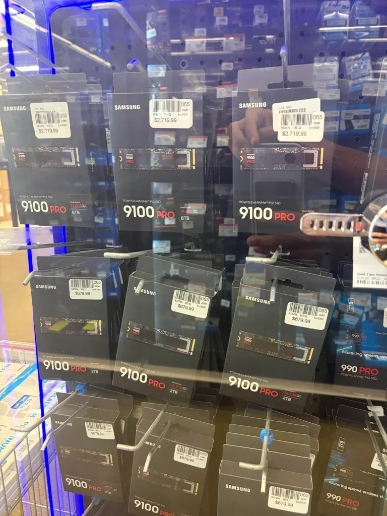 Samsung 9100 PRO SSDs are displayed in a store cabinet, with prices labeled '$2,719.99' for 8TB and '$679.99' for 2TB.