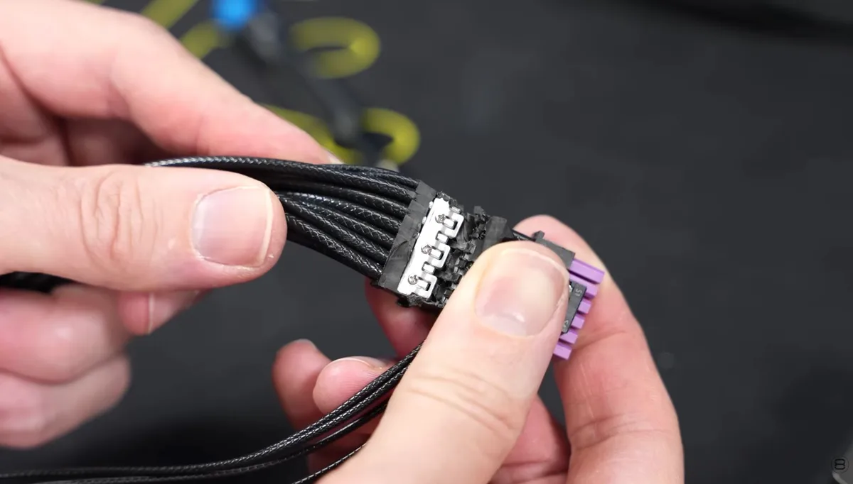 A close-up of a hand holding a black braided cable with a connector featuring four visible pins and purple ends.