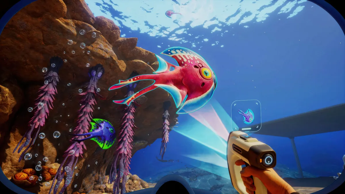 A player in Subnautica aims a scanning tool at a vibrant, alien fish in an underwater environment.