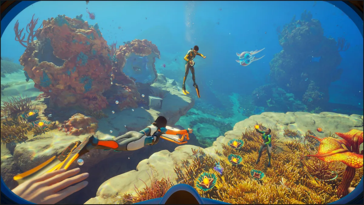 A player in the game'Subnautica 2' explores an underwater landscape with colorful coral and aquatic plants, accompanied by two other divers.