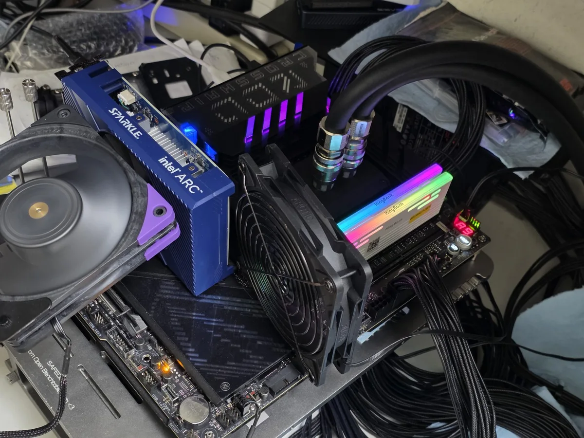 A PC setup features a Sparkle Intel Arc graphics card with a fan, RGB-lit RAM sticks labeled with'Neo Forza,' and liquid cooling tubes connected to the CPU on an open test bench.
