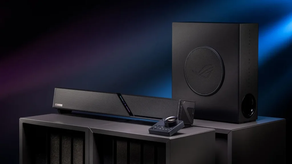 The ROG Gjallar gaming soundbar, control hub and wireless subwoofer sitting on black stands against a blue background.