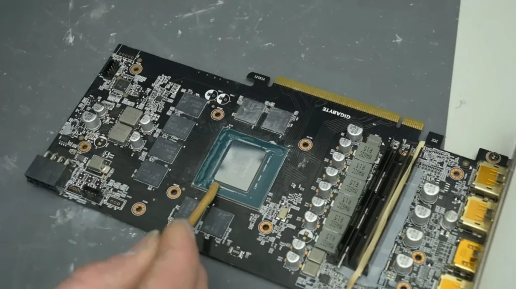 A Gigabyte NVIDIA GeForce graphics card with its GPU exposed and a tool applying thermal paste.