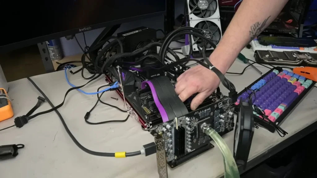 A person is assembling a custom PC with Corsair Vengeance RAM and visible EKWB cooling components on a test bench, next to a colorful mechanical keyboard.