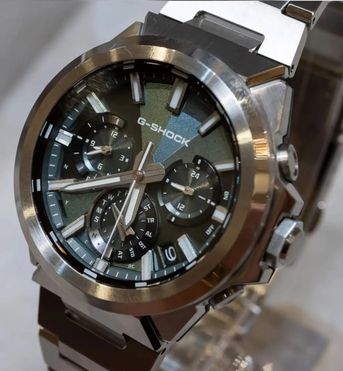 Close-up of the green-dial Casio G-Shock GST-W1000D-3A, showing its geometric textured dial, three subdials, luminous markers, and polished stainless steel bezel.