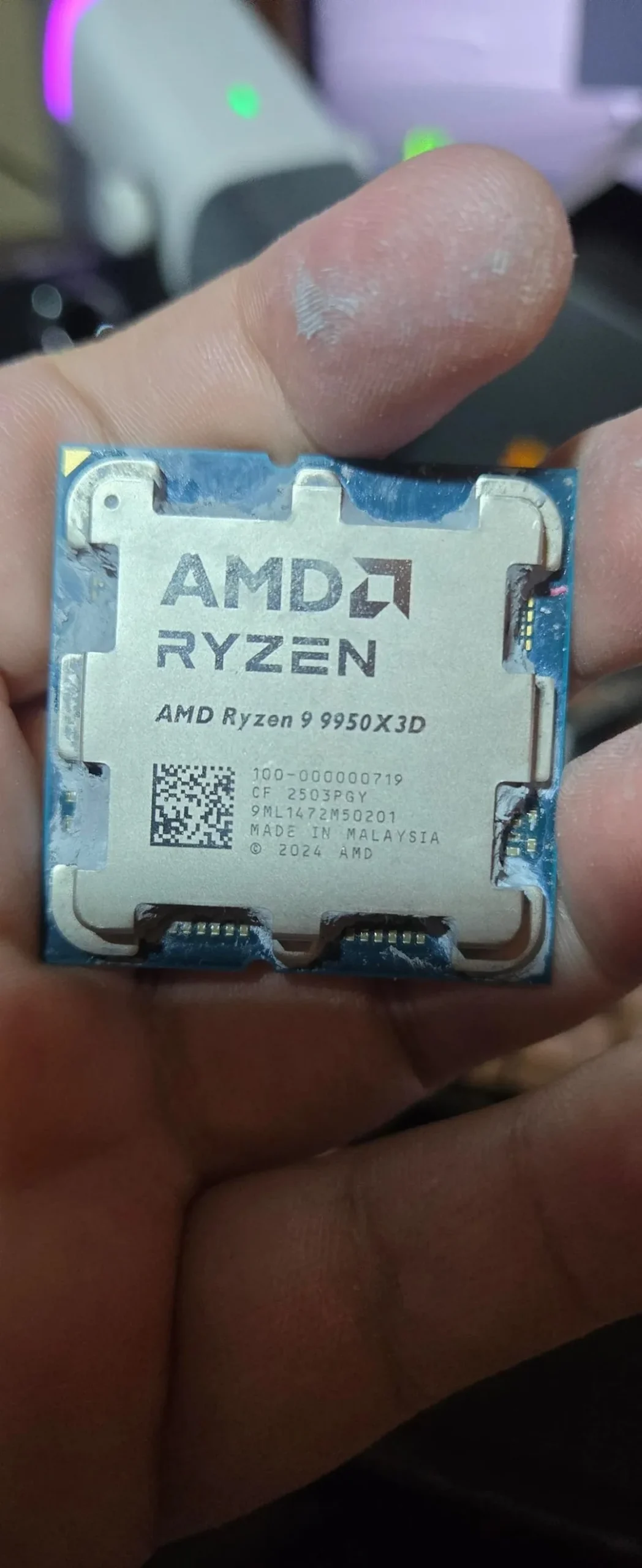 A hand holding an AMD Ryzen 9 9950X3D processor with visible text detailing specifications and manufacturing information.