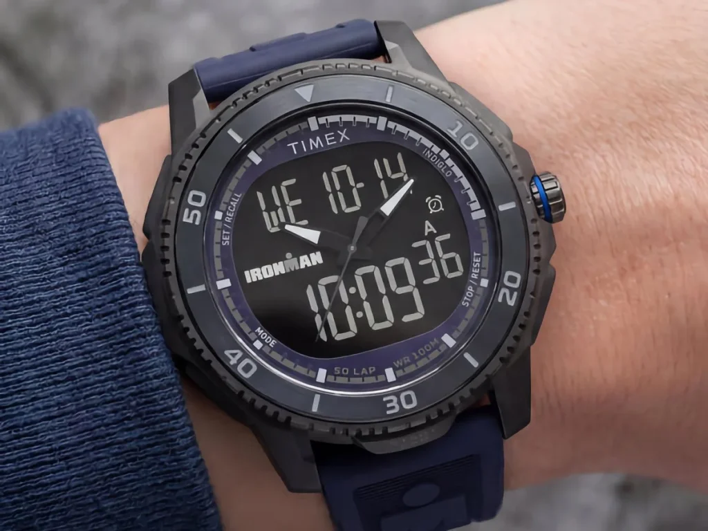 Black Timex Ironman Adrenaline ana-digi watch with a dark blue strap and blue crown accent, shown on a wrist.