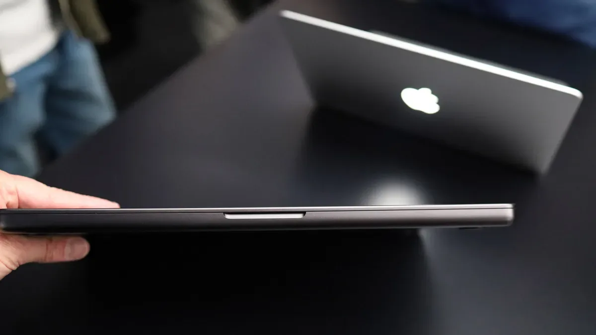 Nuevo MacBook Pro táctil cerrado de canto, con otro modelo detrás mostrando el logo de Apple iluminado